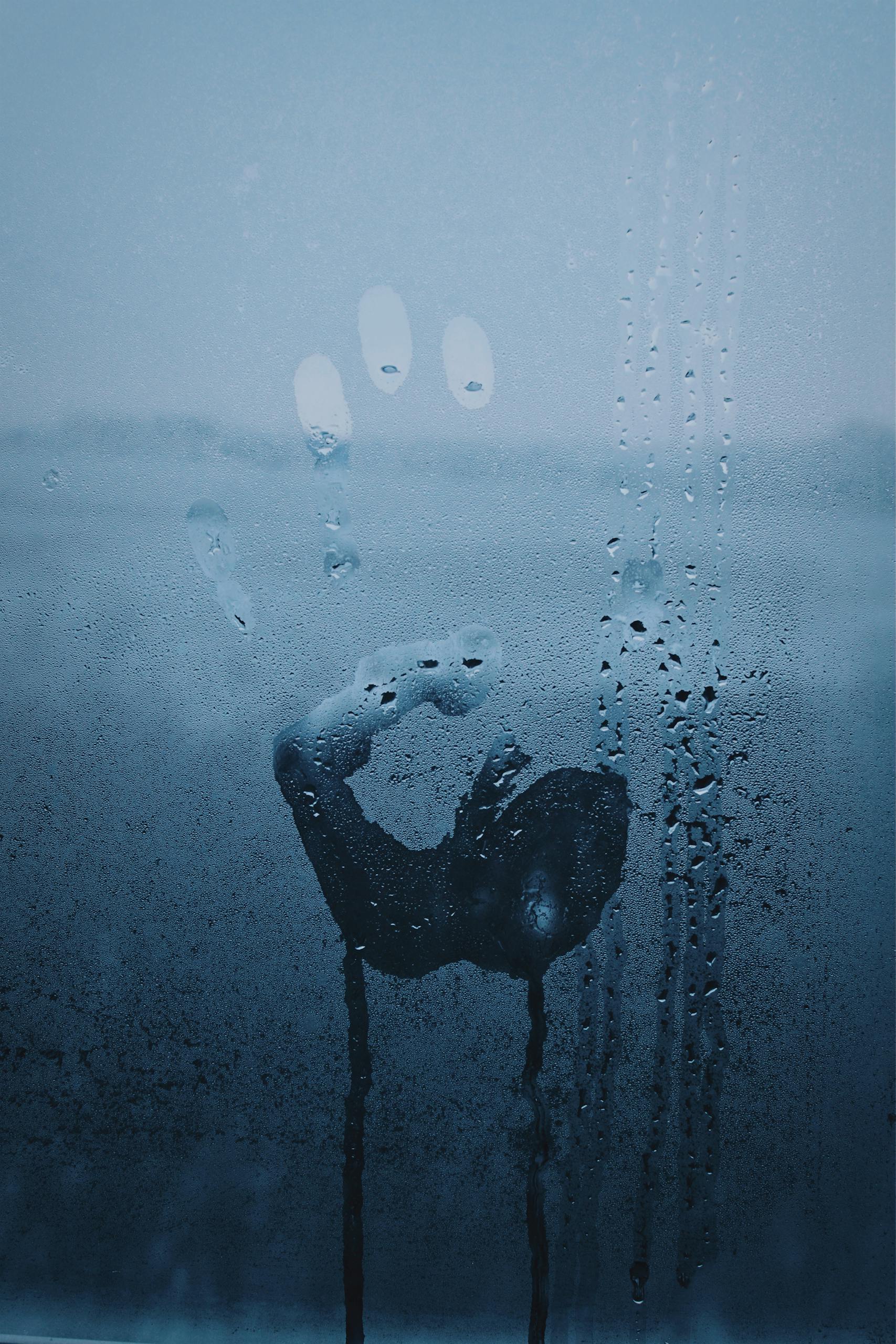 A mysterious handprint on a fogged up glass window, viewed in a close-up shot.