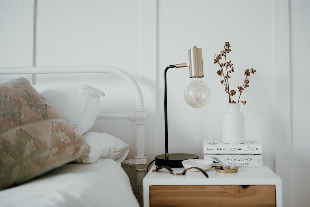 Stylish minimalist bedroom with a modern bedside table featuring a lamp, books, and decorative elements.