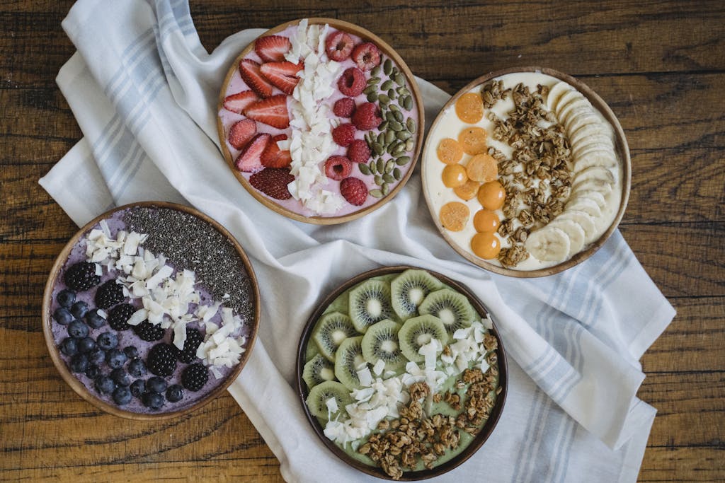 Top view of colorful smoothie bowls with a variety of fresh fruits and toppings on a wooden table.