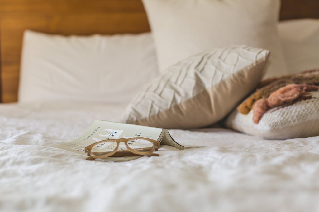 Serene bedroom scene with an open book and reading glasses on a soft bed.