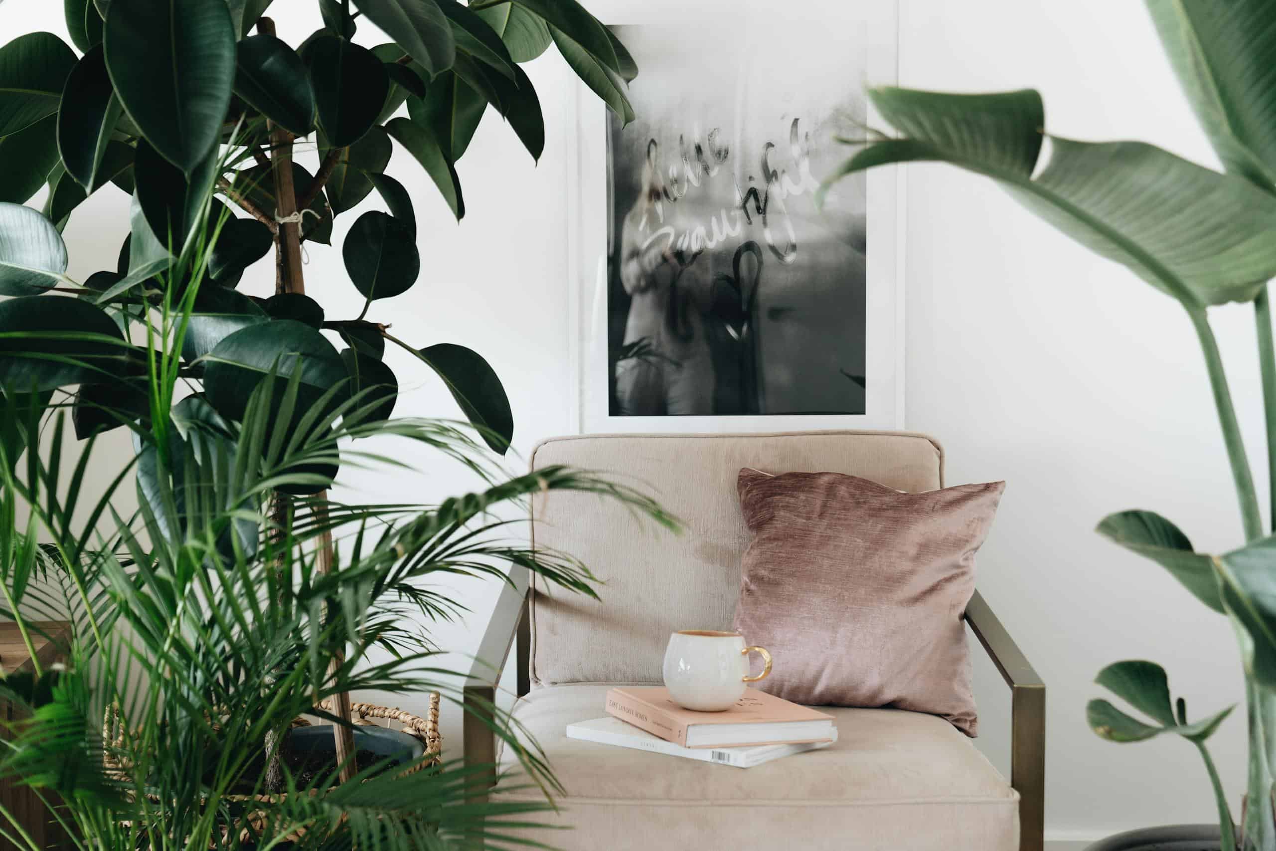 Elegant interior with beige chair, lush plants, and art, creating a serene reading nook.