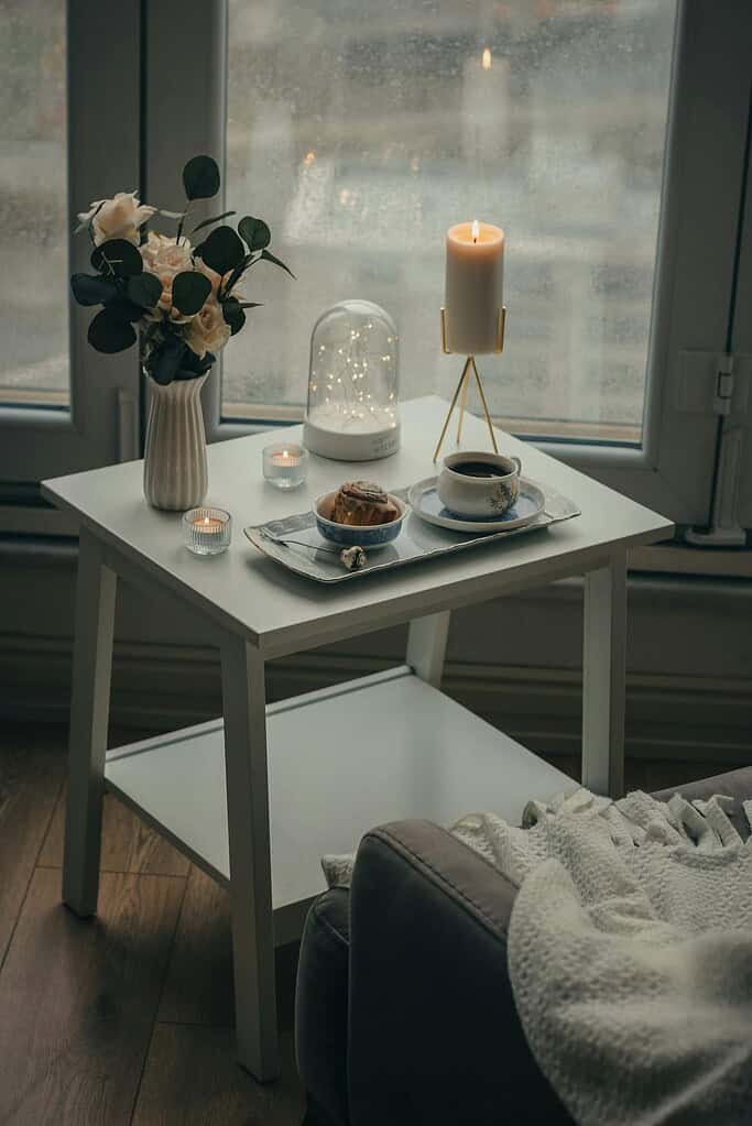 A serene indoor scene with a coffee tray, candle, and flowers on a table by the window.