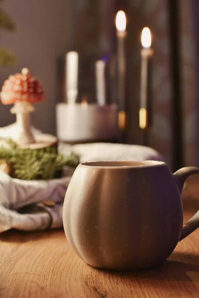 A warm mug set against a backdrop of lit candles and rustic winter decor creates a cozy ambiance.