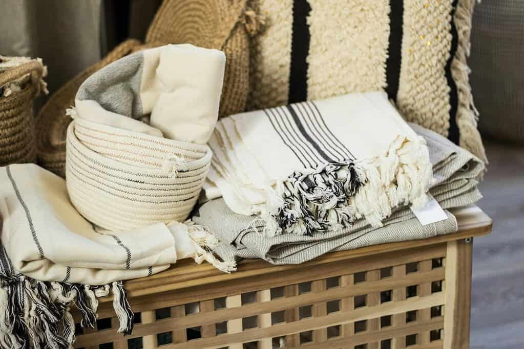 Collection of cozy white towels and plaid stacked on wooden container near wicker baskets in light room