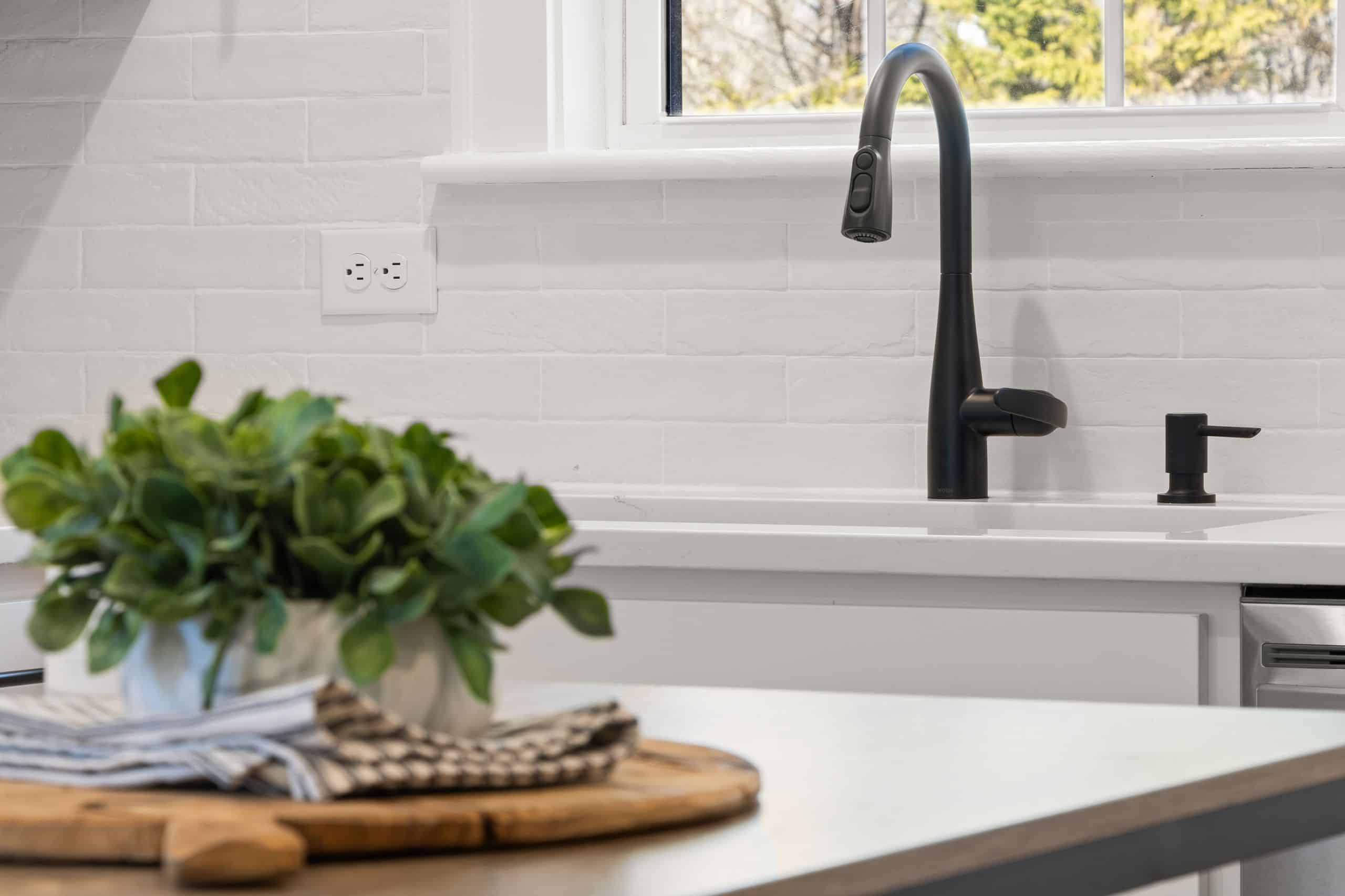 A clutter free kitchen featuring a black faucet, white brick backsplash, and a potted plant on the counter.