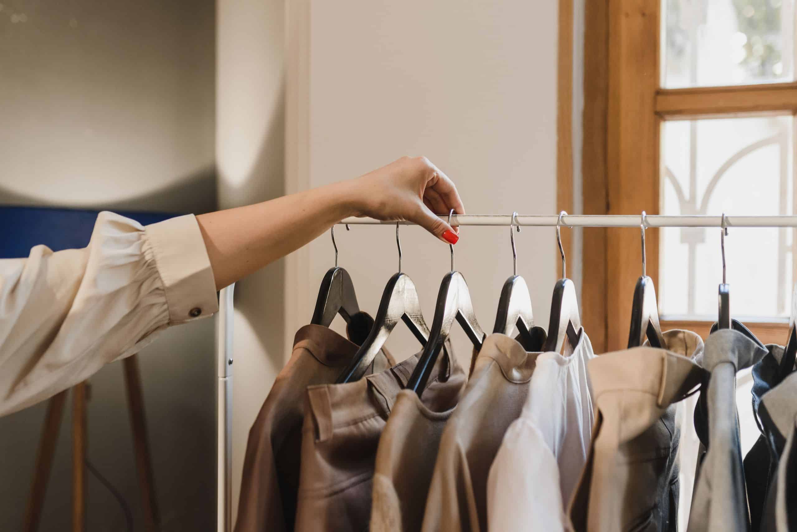 A woman's hand selecting a jacket from an organized rail in her capsule wardrobe