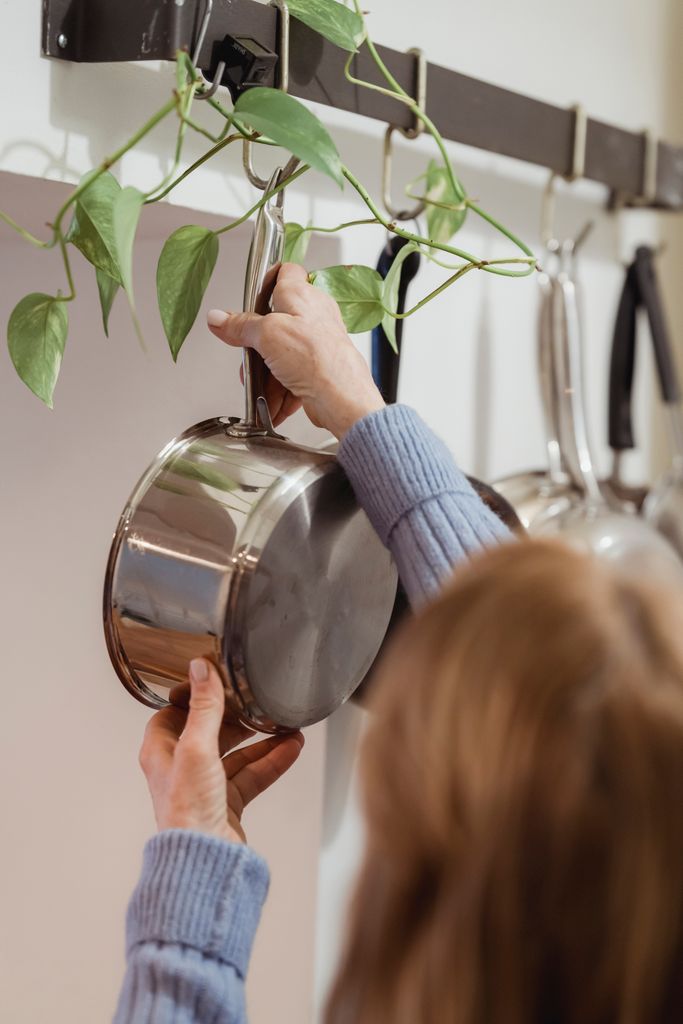 Person hanging a stainless steel non-toxic pot on a wall-mounted rack in a modern kitchen.