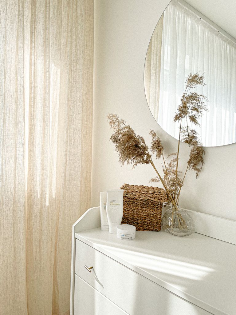 Bright minimalist interior showing dresser, mirror, and dried plants, creating a serene atmosphere.