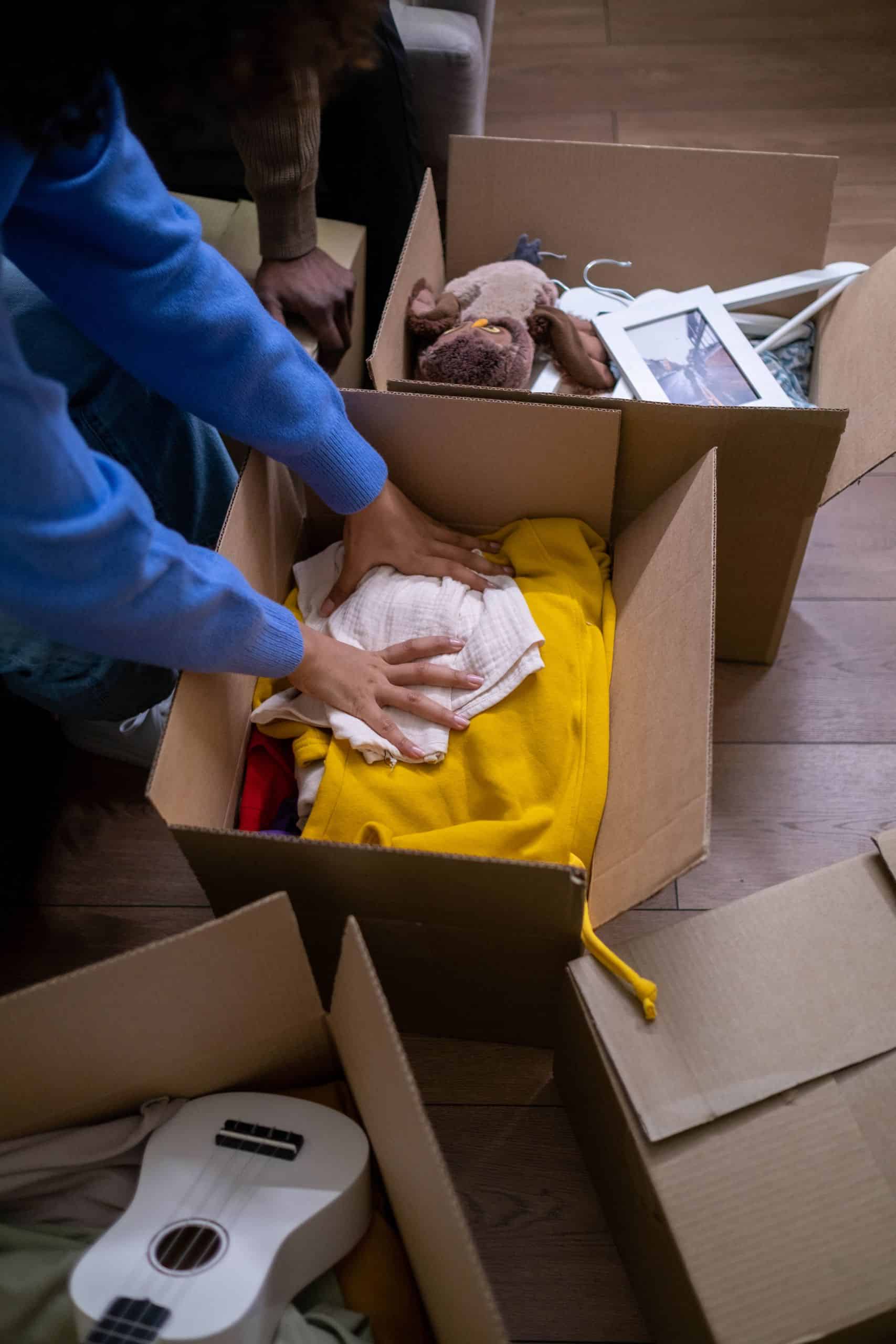 People organizing clothes and toys into cardboard boxes during a decluttering session.