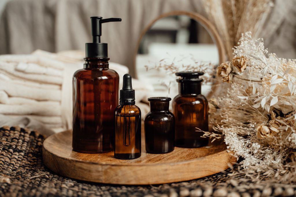 Natural non-toxic skincare set up featuring amber glass bottles on a wooden tray with dried flowers and towels in the background.