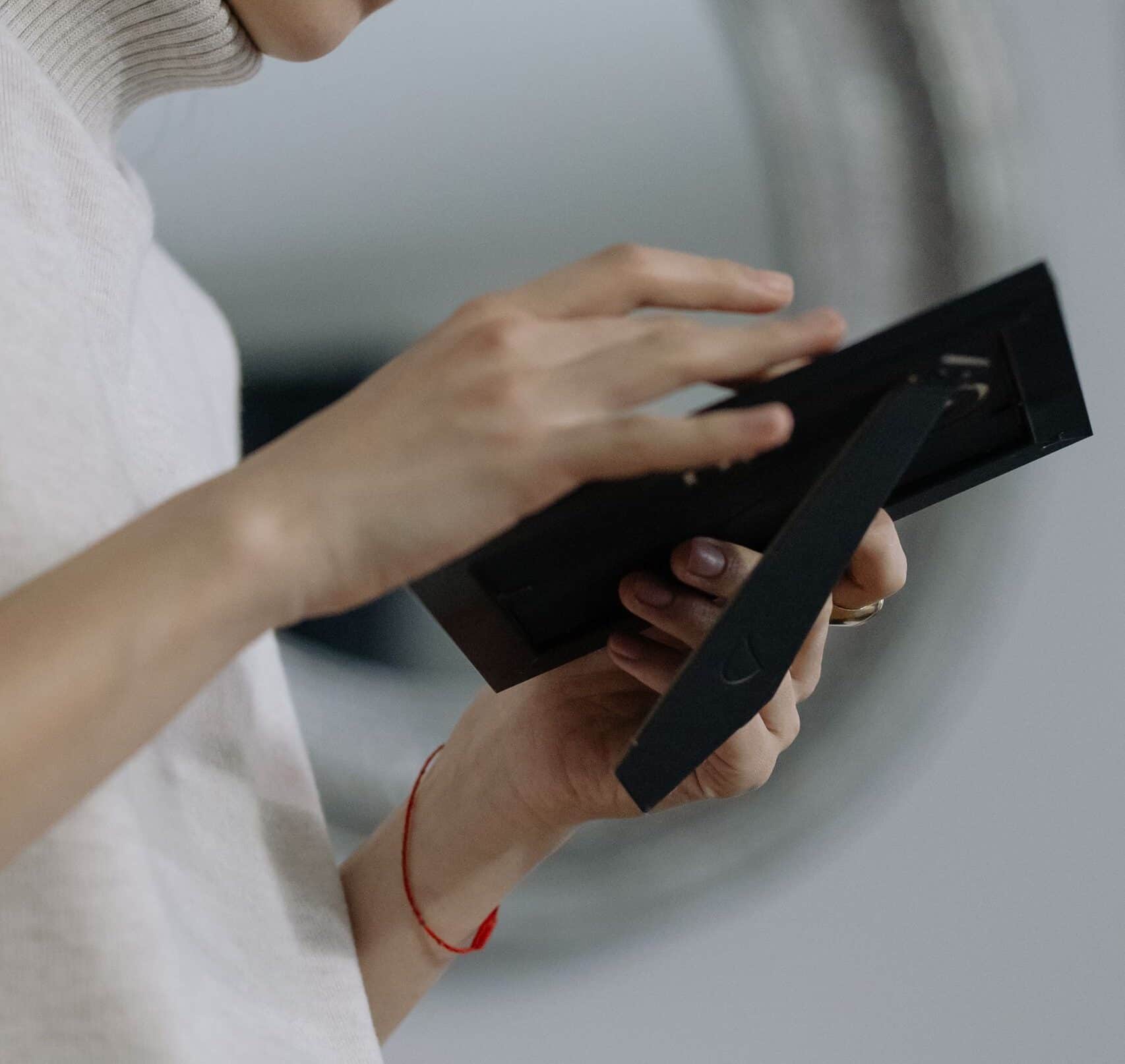 Woman in a turtleneck holding a picture frame, deep in thought, illustrating the challenge of decluttering things that hold emotional weight.