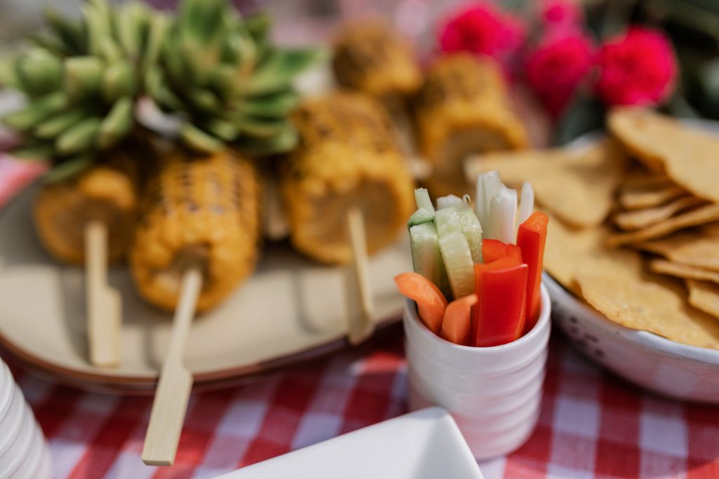 Fresh vegetable sticks, corn on the cob, and tortilla chips on a table as a simple dinner party menu idea