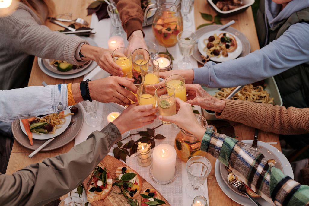 From above of crop friends enjoying dinner with candles while cheering with glasses of drinks illustrating that connection, warmth and laughter are what really make a dinner party memorable