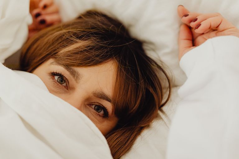 Close-up of a middle-aged woman's open eyes peeking out from under a white bed sheet.