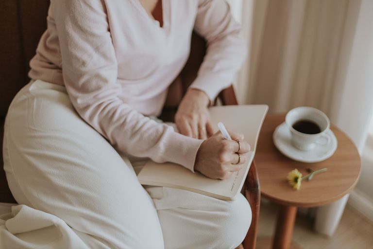 A person with a notebook and coffee cup in in a cozy, bright room illustrating how to do a three day time audit.